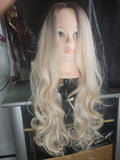 Long wavy wig with a blonde ombre color, displayed on a mannequin head stand in what appears to be a salon or studio setting.